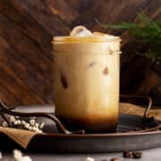 Almond milk latte jar on a tray with coffee beans.