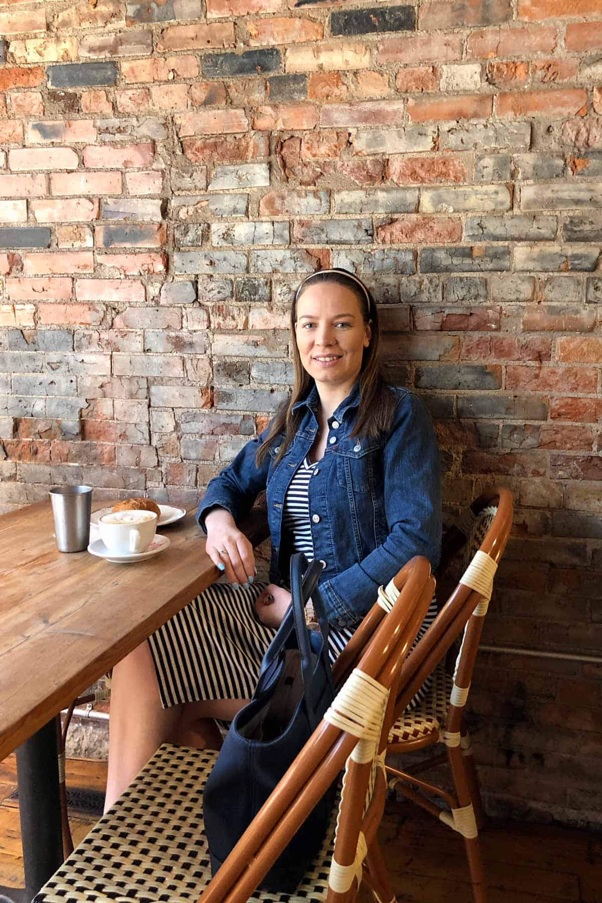 Natasa sitting on a chair in a coffee shop next to a brick wall.