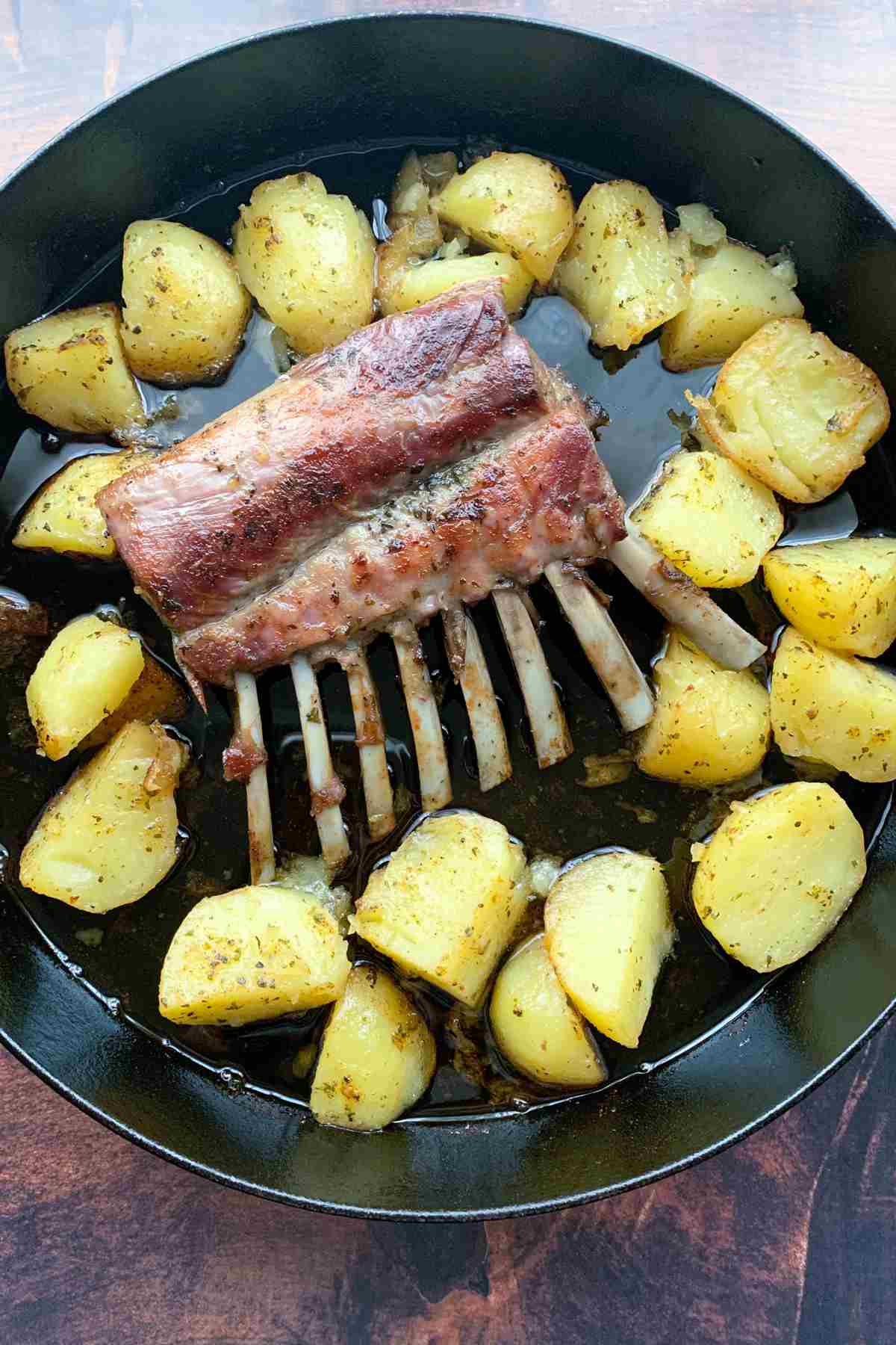 Baked lamb ribs with potato in cast iron skillet overhed.