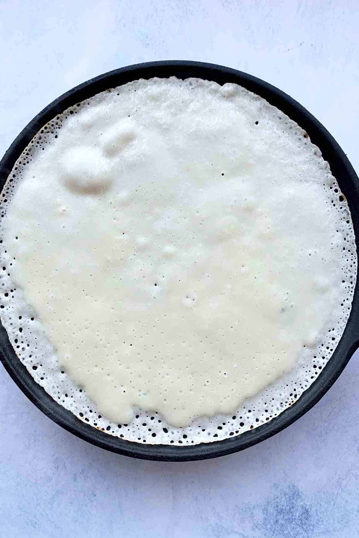 Cooking crepe batter in a pan.