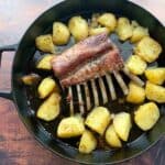 Lamb ribs with baked potato in cast iron skillet overhead.