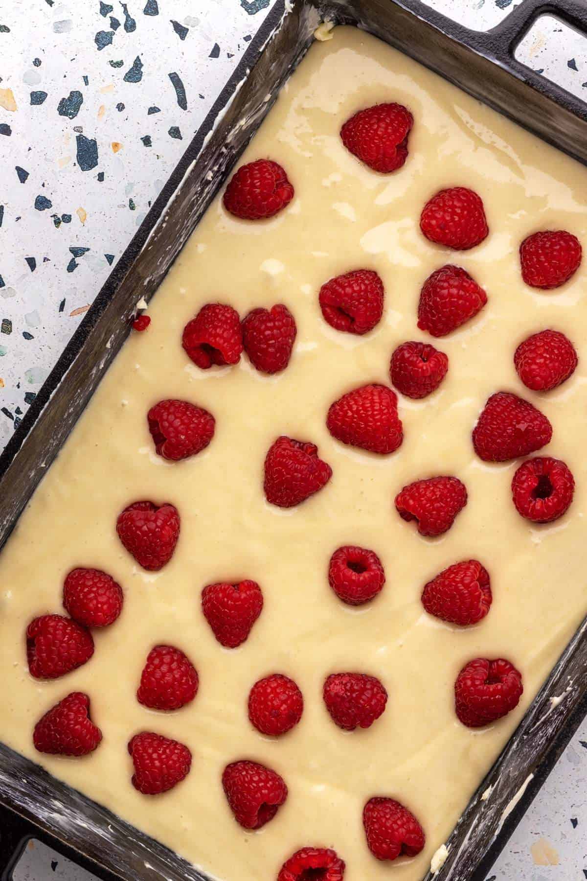 Cake batter with raspberries on top in cast iron skillet.