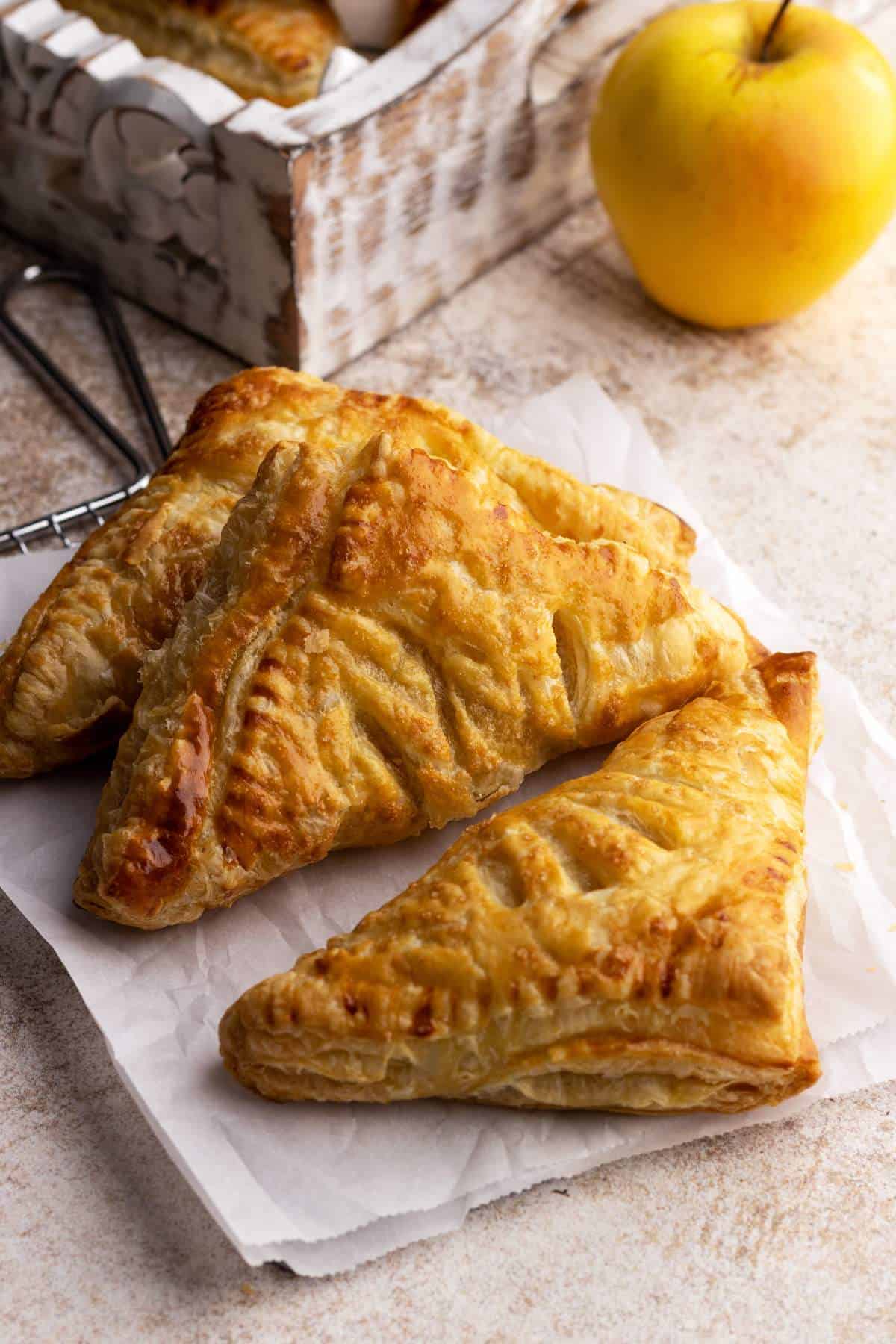 Apple turnovers on a wire rack with an apple in the background.