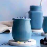Blue spirulina in a small jar on a marble coaster.