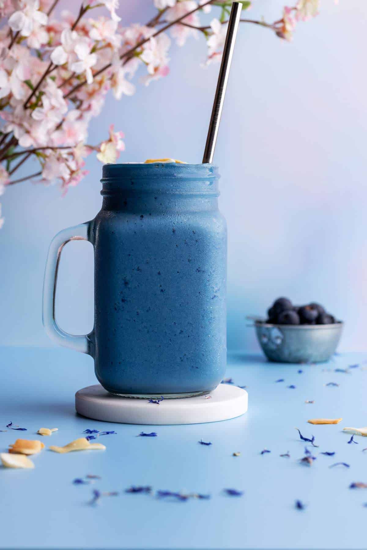 Blue spirulina smoothie in a tall jar on a coaster.