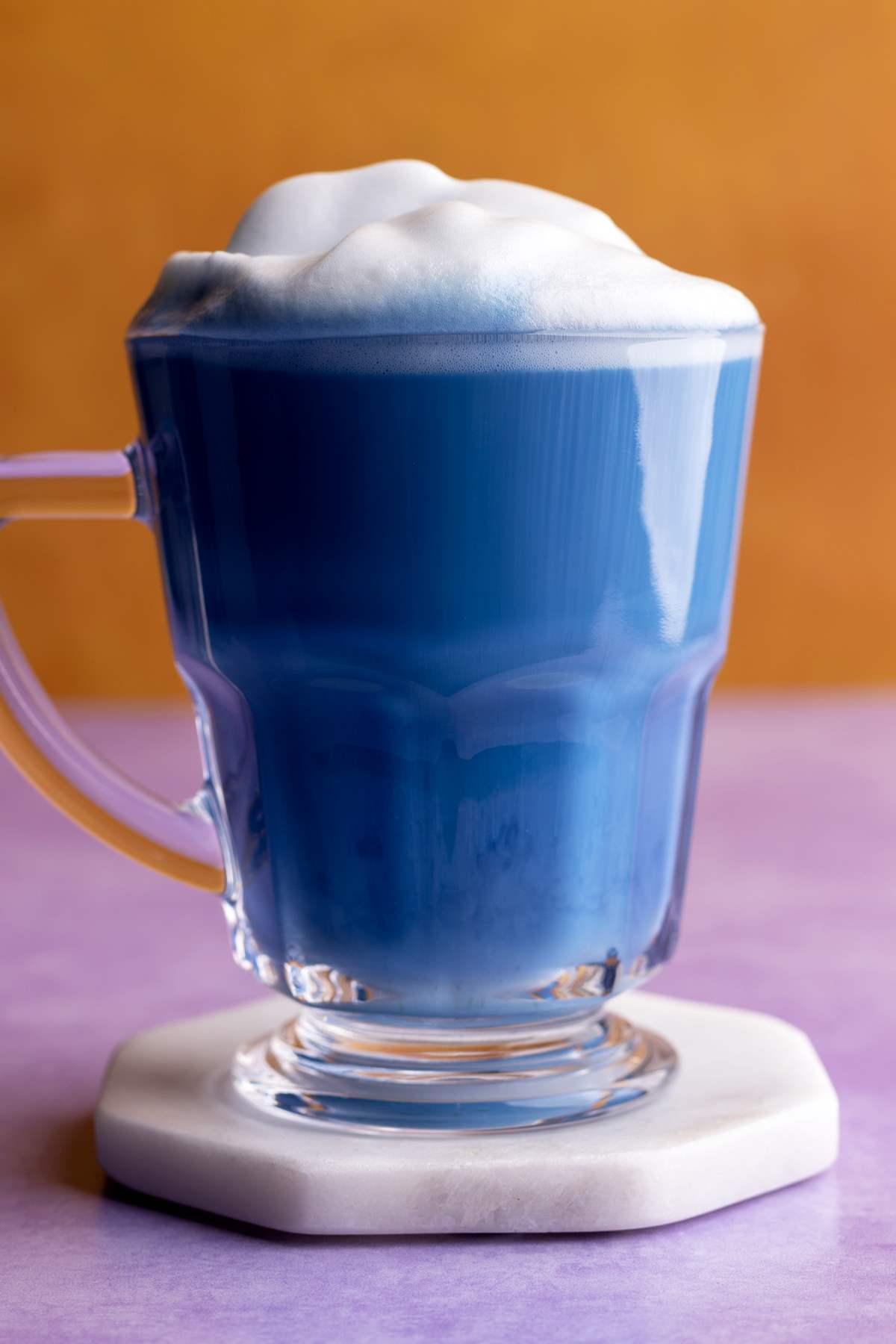 Butterfly pea latte in glass mug on a coaster.