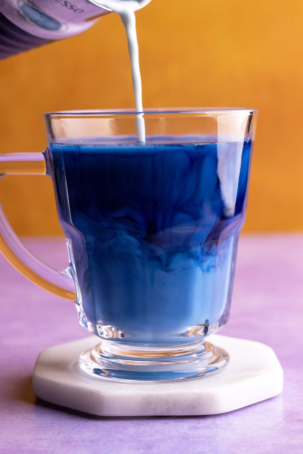 Butterfly pea latte pouring into glass mug.