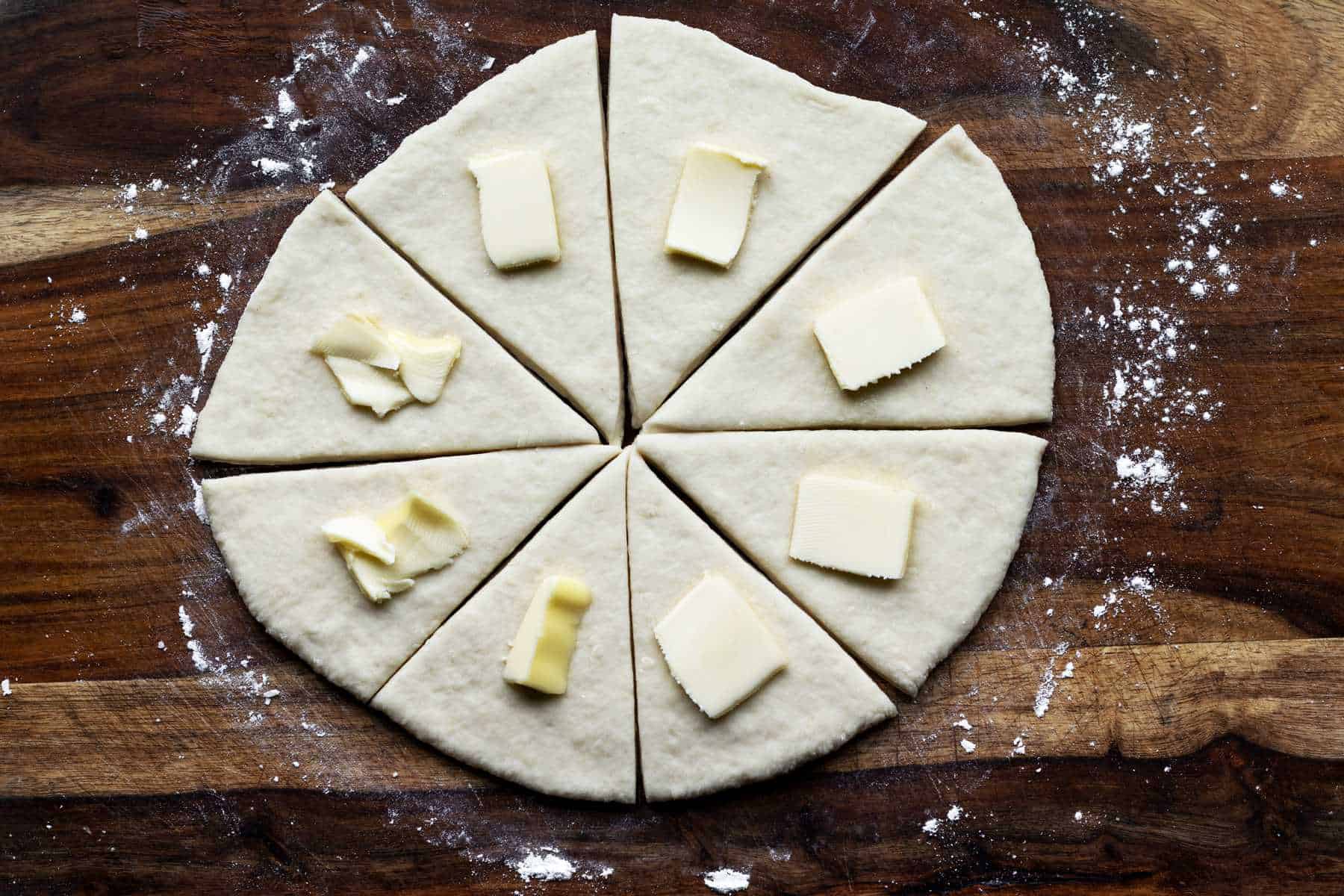 Dough divided into eight triangles with little pieces of butter on top.