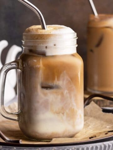 Frothy iced oat milk latte in a jar closeup shot.