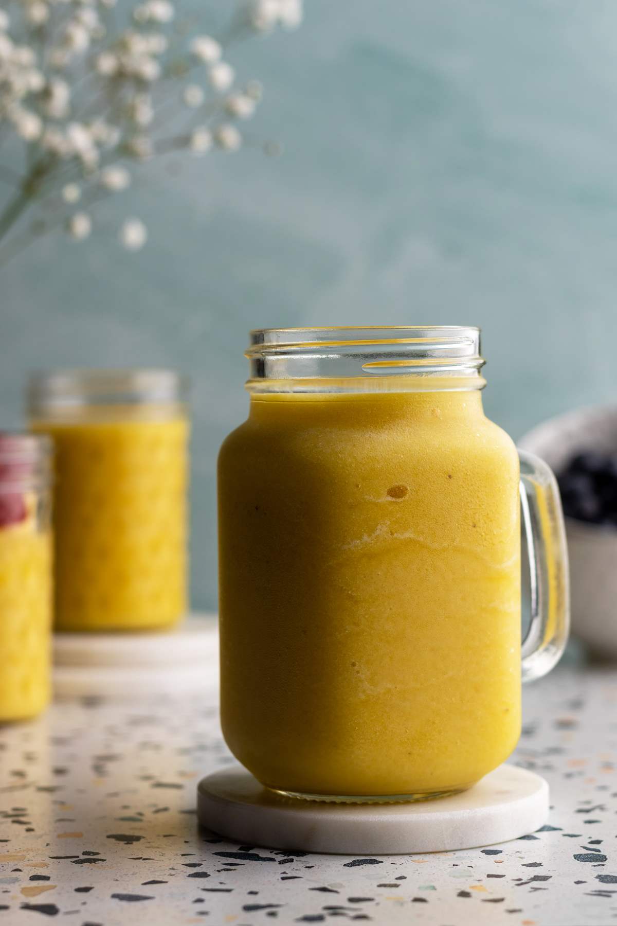 Pineapple mango smoothie in a jar on a coaster.