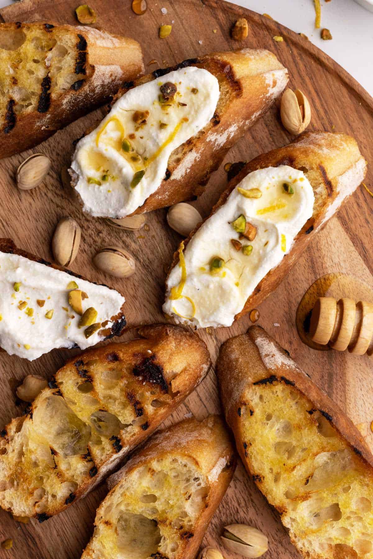 Honey ricotta toast with pistachios on wooden board.
