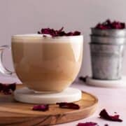 Rose chai latte in a glass cup on a coaster and wooden board.