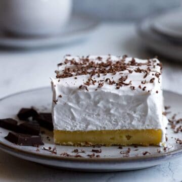 Lemon meringue slice on a plate with chocolate pieces.