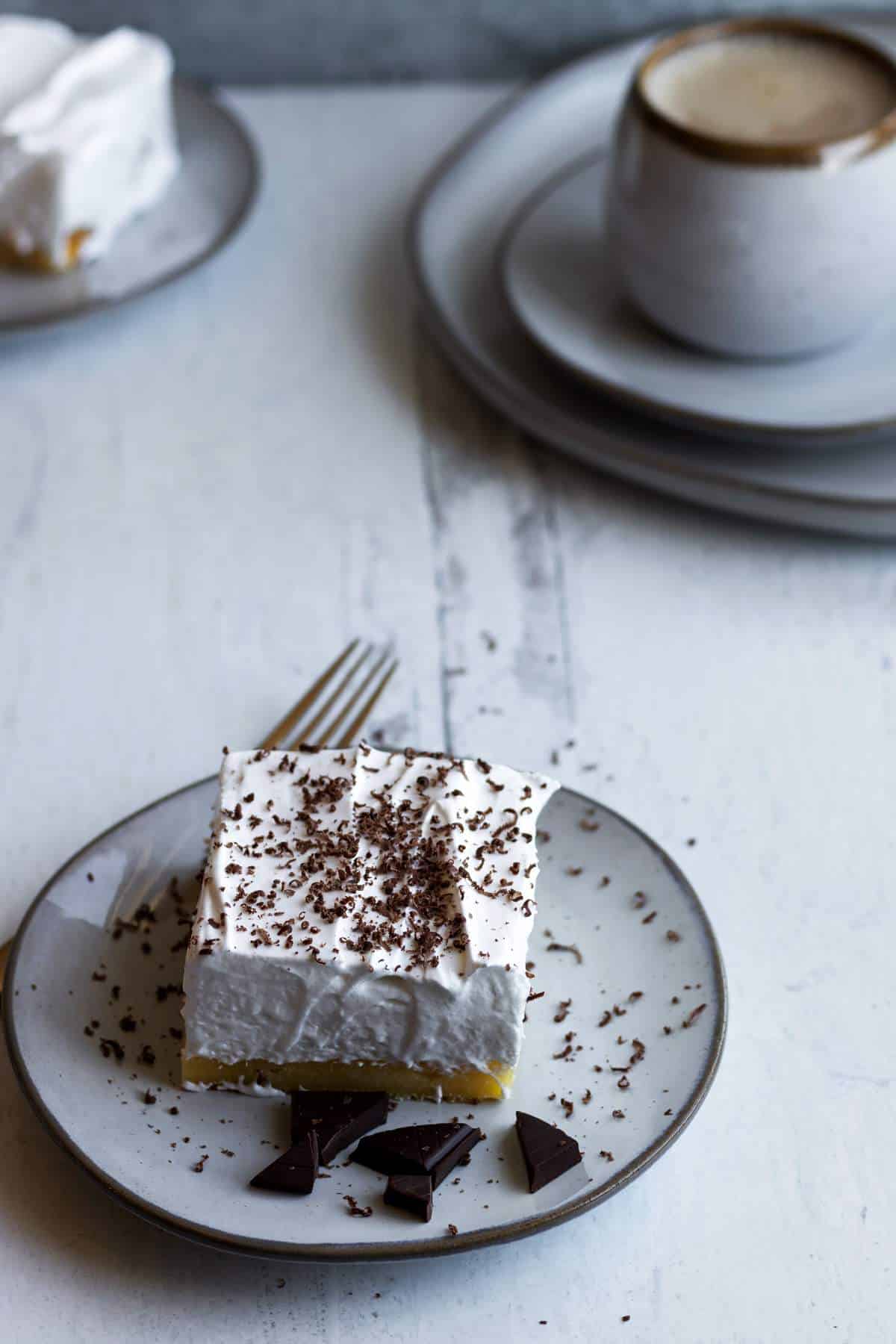 Lemon meringue slice on a plate with chocolate pieces.