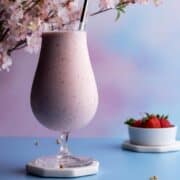 Strawberry banana milkshake in glass on coaster.