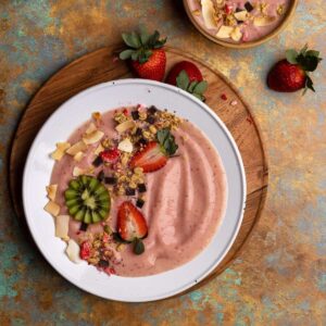 Strawberry smoothie bowl on wooden plate overhead.