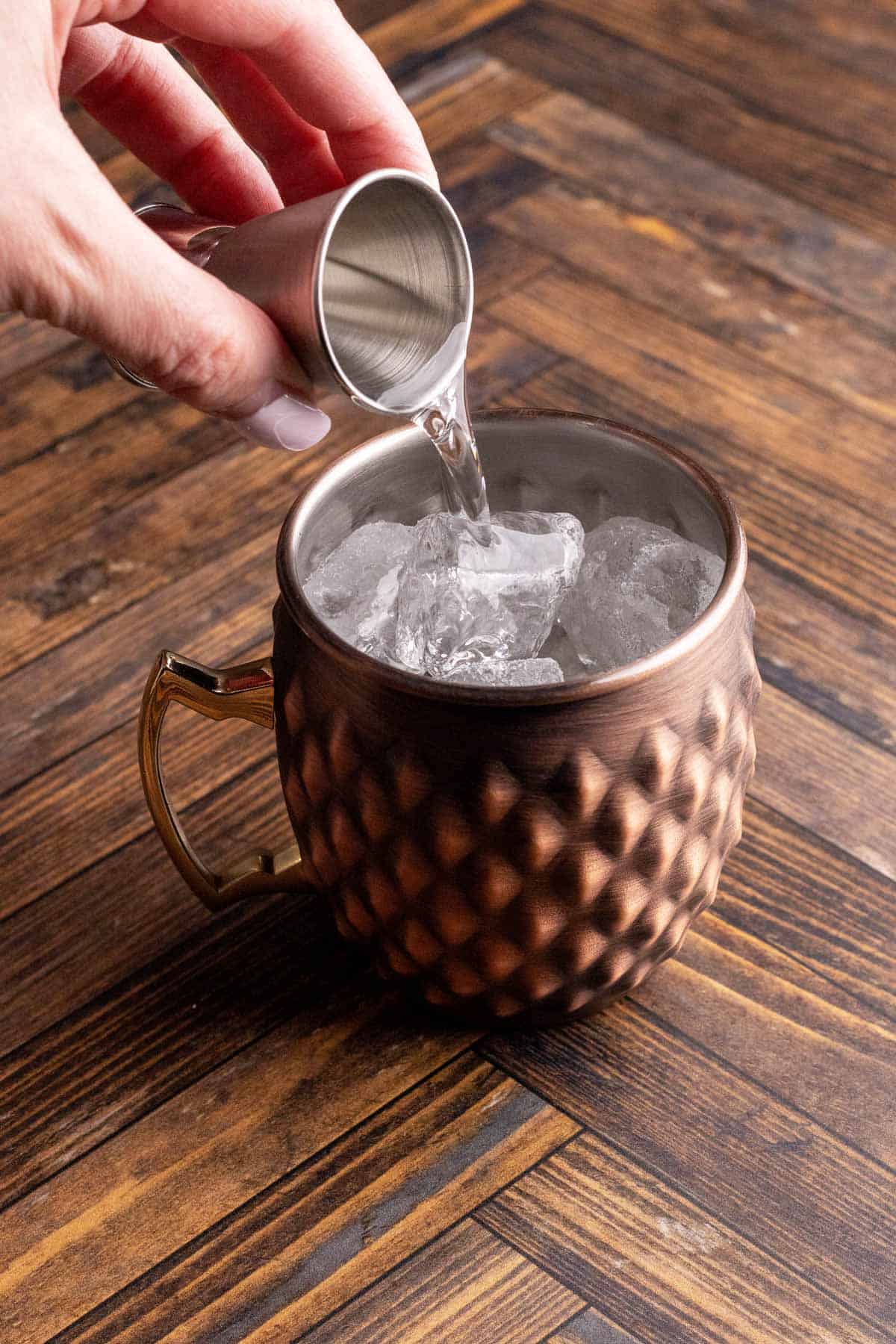 Adding gin to copper mug with ice.