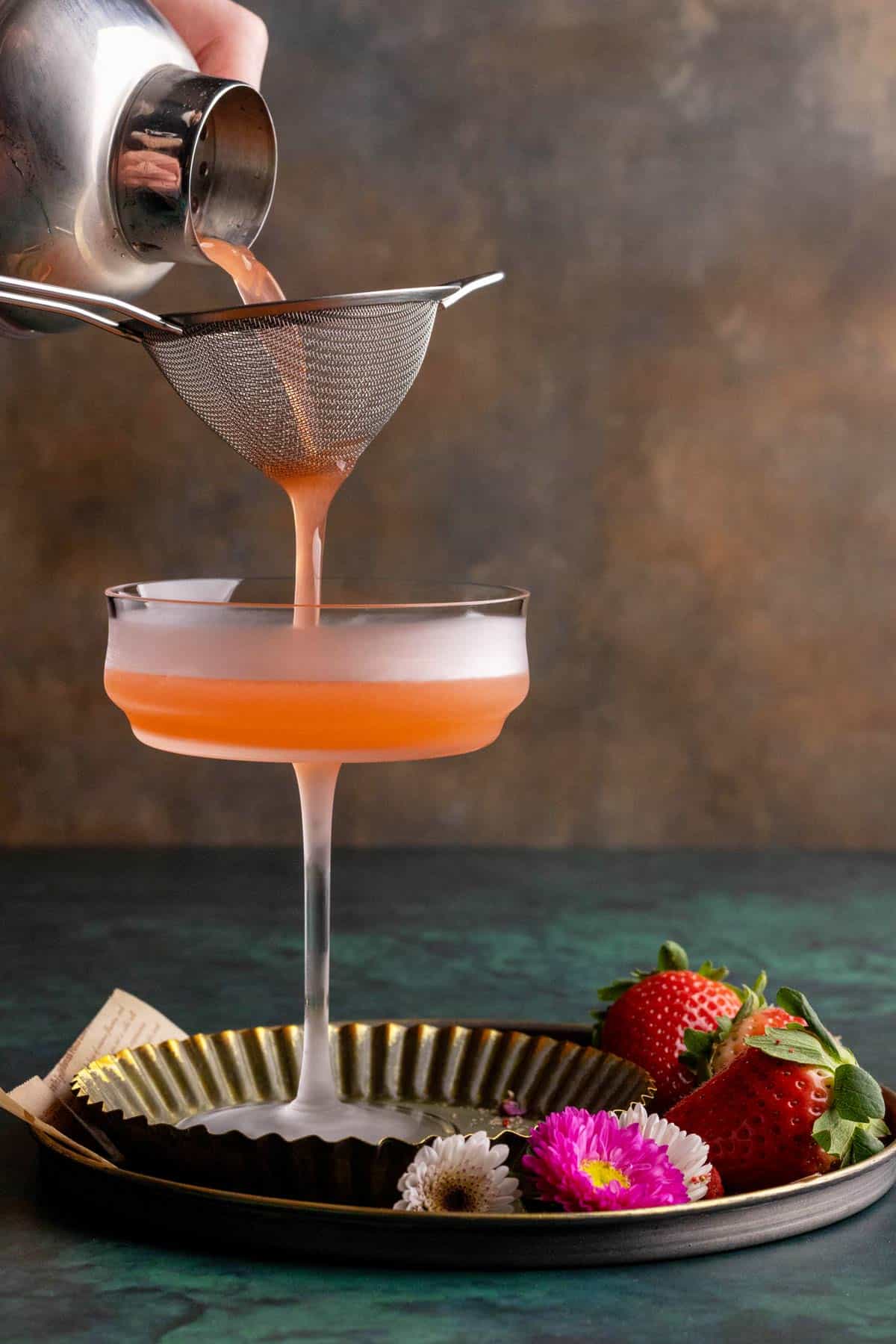 Double-straining strawberry martini into a chilled glass.