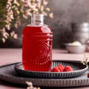 Raspberry simple syrup in a syrup dispenser on metal plates.
