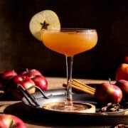 Apple cider vodka martini on a tray with apples and spices.