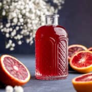 Blood orange syrup in dispenser surrounded with fresh blood oranges.