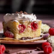 Raspberry cake with whipped cream and grated chocolate on a plate with parchment paper.
